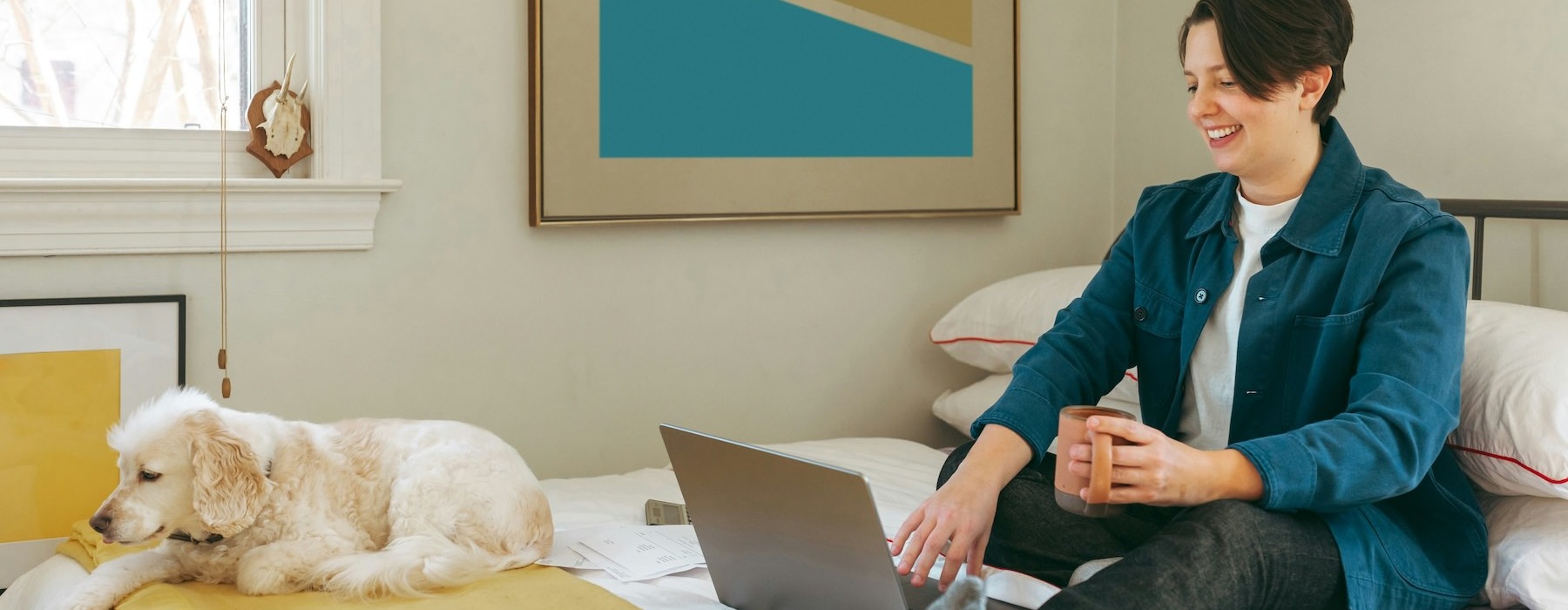 a person sitting on a bed with a laptop and a dog