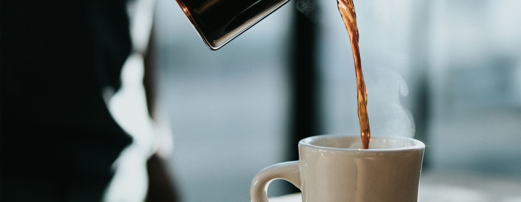 a person pouring a carafe of coffee into a cup